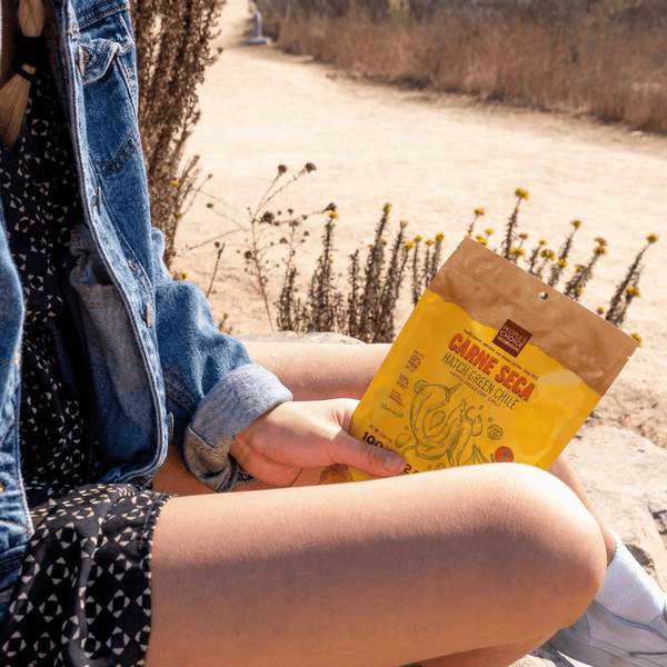 Person holding beef jerky outdoors with natural scenery