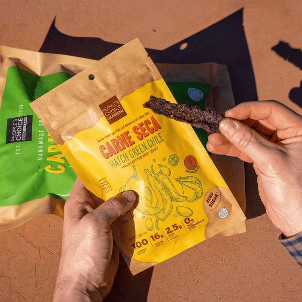 Person holding a yellow 'Carne Seca' package with a snack, against a brown background