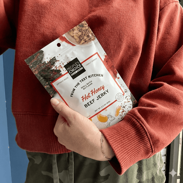 Person holding a package of hot honey beef jerky against a red sweater background