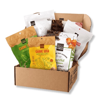 A cardboard gift box filled with assorted packaged snacks and jerky from Choice Choice Restaurants and Carne Seca, photographed on a clean white background.